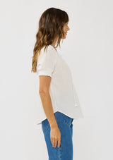 [Color: White] A side facing image of a brunette model wearing a lightweight white top with puff sleeves and a split neckline with tassel ties. 