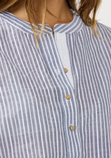 [Color: Blue/White] A detail image of a brunette model wearing a blue and white striped top with rolled cap sleeves, a button front, and a mandarin collar.  