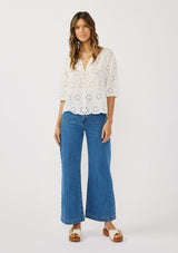 [Color: White] A front facing image of a brunette model wearing a white eyelet embroidered top with half sleeves and a button front. A classic spring top styled with denim. 