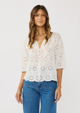 [Color: White] A front facing image of a brunette model wearing a white eyelet embroidered top with half sleeves and a button front. A classic spring top styled with denim. 