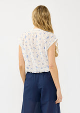 [Color: White/Blue] A back facing image of a blonde model wearing a white and blue floral top with a v neckline, short dolman sleeves, and an elastic hem at the back. 
