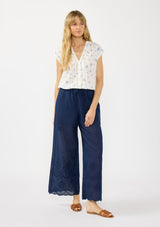 [Color: White/Blue] A front facing image of a blonde model wearing a white and blue floral top with a v neckline, short dolman sleeves, and an elastic hem at the back. 