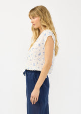 [Color: White/Blue] A side facing image of a blonde model wearing a white and blue floral top with a v neckline, short dolman sleeves, and an elastic hem at the back. 