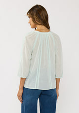 [Color: Mint] A back facing image of a brunette model wearing a sheer mint blouse with lace trims and a hidden button front.