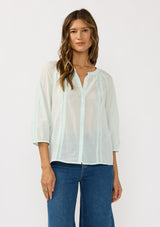 [Color: Mint] A front facing image of a brunette model wearing a sheer mint blouse with lace trims and a hidden button front.