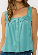 [Color: Teal] A detail image of a brunette model wearing a bohemian teal tank top with a button front, square neckline, and wide straps with ruffle trims. 