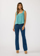 [Color: Teal] A front facing image of a brunette model wearing a bohemian teal tank top with a button front, square neckline, and wide straps with ruffle trims. 