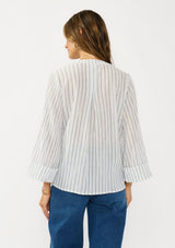 [Color: White/Denim Blue] A back facing  image of a brunette model wearing a blue and white striped blouse with a v neckline, button front, and long wide sleeves. 