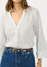 [Color: White/Denim Blue] A detail image of a brunette model wearing a blue and white striped blouse with a v neckline, button front, and long wide sleeves. Styled tucked in with dark wash denim 