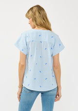 [Color: Blue/White] A back facing image of a blonde model wearing a blue striped top with embroidery, a v neckline, and short dolman sleeves.