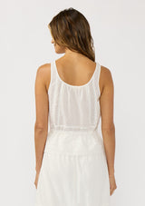 [Color: White] A back facing image of a brunette model wearing a white cotton tank top with an eyelet trimmed hem, a drawstring waist, and a round neck with tie detail. Styled with a matching white maxi skirt. 