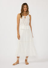 [Color: White] A front facing image of a brunette model wearing a white cotton tank top with an eyelet trimmed hem, a drawstring waist, and a round neck with tie detail. Styled with a matching white maxi skirt. 