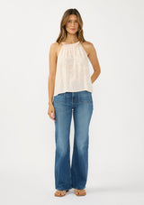 [Color: Shell/Cream] A front facing image of a brunette model wearing a light beige floral sleeveless top with a tie back detail. Styled with a dark wash denim with patch pockets. 