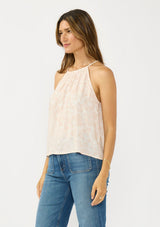 [Color: Shell/Cream] A side facing image of a brunette model wearing a light beige floral sleeveless top with a tie back detail.