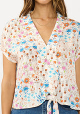[Color: Ivory/Orange] A detail image of a brunette model wearing an ivory and orange floral boho top with short sleeves, a v neckline, and a tie front detail.