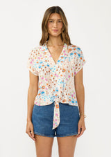 [Color: Ivory/Orange] A front facing image of a brunette model wearing an ivory and orange floral boho top with short sleeves, a v neckline, and a tie front detail.