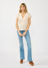 [Color: Natural] A front facing image of a blonde model wearing a lightweight beige top with embroidered cutouts, pintucks, and a v neckline.