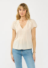 [Color: Natural] A front facing image of a blonde model wearing a lightweight beige top with embroidered cutouts, pintucks, and a v neckline. 