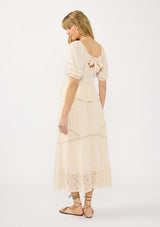 [Color: Natural] A back facing image of a blonde model wearing a beige puff sleeve top with a square neckline, lace front, pintuck details, and a tie back detail. Styled with a matching beige lace maxi skirt.