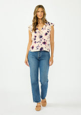 [Color: Peach/Plum] A front facing image of a brunette model wearing a pink and purple floral top with flutter sleeves, a v neckline with ruffle trim, and a tie front detail. 