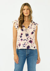 [Color: Peach/Plum] A front facing image of a brunette model wearing a pink and purple floral top with flutter sleeves, a v neckline with ruffle trim, and a tie front detail. 