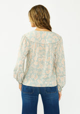 [Color: Dusty Sage/Natural] A back facing image of a brunette model wearing a mint floral blouse with a v neckline, front yoke, and long sleeves. Paired with a dark wash denim with patch pockets. 