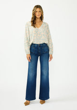 [Color: Dusty Sage/Natural] A front facing image of a brunette model wearing a mint floral blouse with a v neckline, front yoke, and long sleeves. Paired with a dark wash denim with patch pockets. 