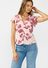 [Color: Coral/Wine] A front facing image of a brunette model wearing a pink and wine floral print top with a ruched center, short flutter sleeves, and a v neckline. 