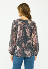 [Color: Grey/Dusty Rose] A back facing image of a brunette model wearing a relaxed peplum top with a floral print, clipped lurex, and a v neckline with tie detail. 