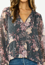 [Color: Grey/Dusty Rose] A detail image of a brunette model wearing a relaxed peplum top with a floral print, clipped lurex, and a v neckline with tie detail. 