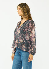 [Color: Grey/Dusty Rose] A side facing image of a brunette model wearing a relaxed peplum top with a floral print, clipped lurex, and a v neckline with tie detail. 