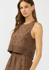 [Color: Brown] A side facing image of a brunette model wearing a brown crop tank top with tonal embroidery and a round neckline.