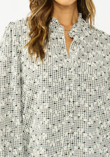 [Color: Black] A detail image of a brunette model wearing a black and white checkered pattern blouse with embroidered details and a button front. 