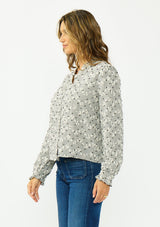 [Color: Black] A side facing image of a brunette model wearing a black and white checkered pattern blouse with embroidered details and a button front. 
