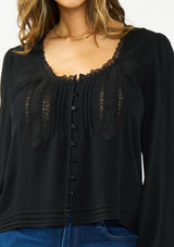 [Color: Black] A detail image of a brunette model wearing a black lace long sleeve top with a scoop neckline and button front. 
