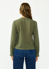[Color: Olive] A back facing image of a brunette model wearing an olive green embroidered blouse with a button front and a button cuff closure with ruffle trim. Paired with a dark wash denim.