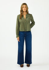 [Color: Olive] A front facing image of a brunette model wearing an olive green embroidered blouse with a button front and a button cuff closure with ruffle trim. Paired with a dark wash denim and brown ballet flats. 