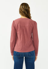 [Color: Rose Brown] A back facing image of a brunette model wearing a bohemian embroidered blouse with lace and pintuck details. Paired with a dark wash denim. 