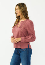 [Color: Rose Brown] A side facing image of a brunette model wearing a bohemian embroidered blouse with lace and pintuck details. Paired with a dark wash denim. 