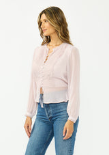 [Color: Lilac] A side facing image of a brunette model wearing a sheer lilac top with a front lace accent, button front, long sleeves, and a tie front waist detail. 