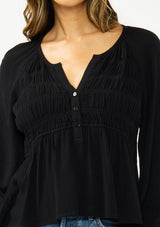 [Color: Black] A detail image of a brunette model wearing a black long sleeve top with a shirred bust area. 