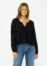 [Color: Black] A front facing image of a brunette model wearing a black long sleeve top with a shirred bust area. 