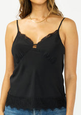 [Color: Black] A detail image image of a brunette model wearing a black lace cami with spaghetti straps. Styled with dark wash denim. 