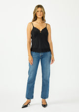 [Color: Black] A front facing image image of a brunette model wearing a black lace cami with spaghetti straps. Styled with dark wash denim. 