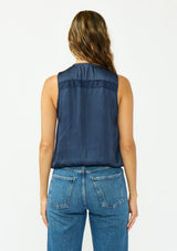 [Color: Midnight] A back facing image of a brunette model wearing a blue satin sleeveless top with an embroidered trim, elastic hem, and a surplice front. 
