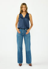 [Color: Midnight] A front facing image of a brunette model wearing a blue satin sleeveless top with an embroidered trim, elastic hem, and a surplice front. 