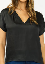 [Color: Black] A detail image of a brunette model wearing a black satin top with an embroidered trim and short dolman sleeves. 