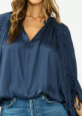 [Color: Midnight] A detail image of a brunette model wearing a relaxed blue satin blouse with ruched sleeves and an elastic hem. 