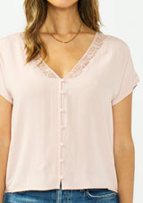 [Color: Shell] A detail image of a brunette model wearing a pink lace trim top with short dolman sleeves and a button front. 