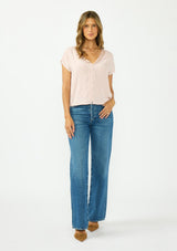 [Color: Shell] A front facing image of a brunette model wearing a pink lace trim top with short dolman sleeves and a button front. Paired with a dark wash denim and brown suede heels. 